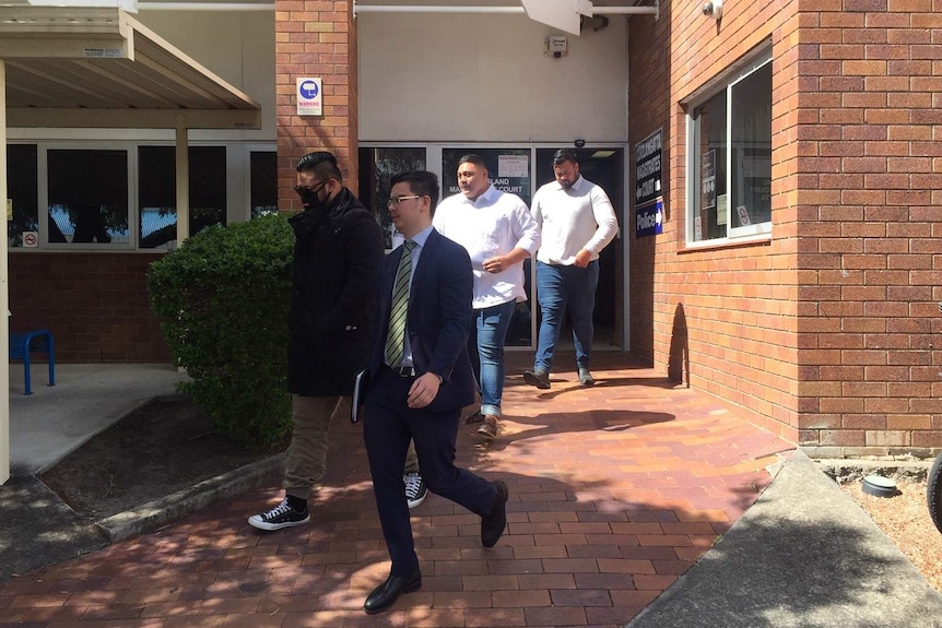 Three men leave court with a man in a suit.