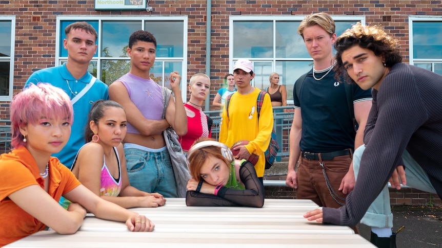 The cast of Heartbreak High pose on set in colourful outfits.