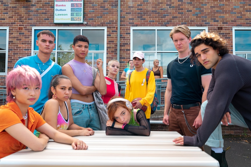 The cast of Heartbreak High pose on set in colourful outfits.