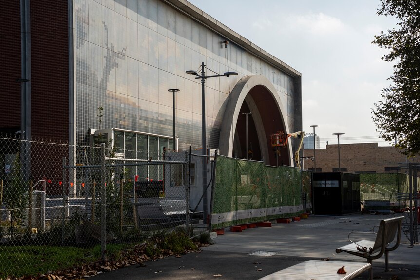 A large building with an arched entrance and temporary fencing around. 