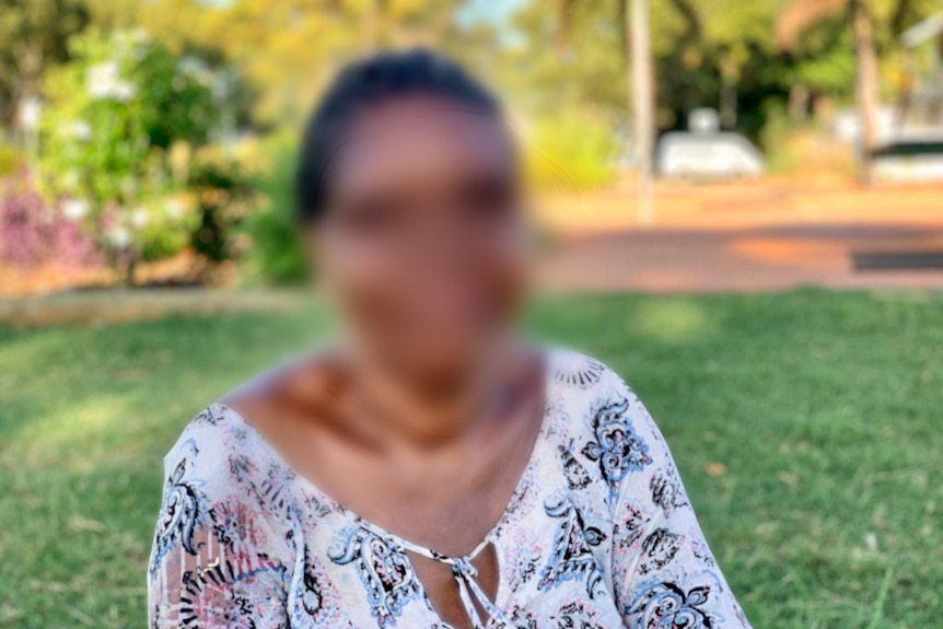 A woman sits in a park smile pensively at the camera.