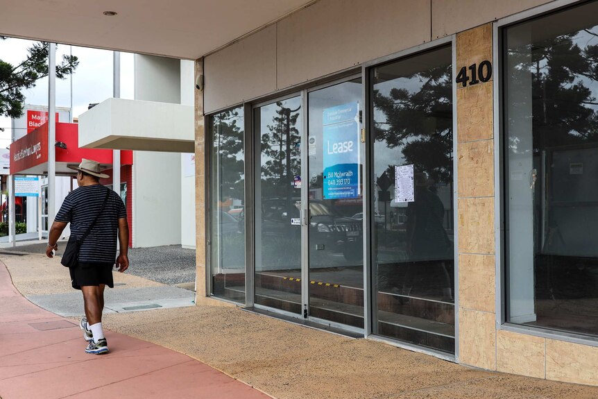 A man walks past an empty shop on Gympie Road at Strathpine with 'Lease' signs in the window.
