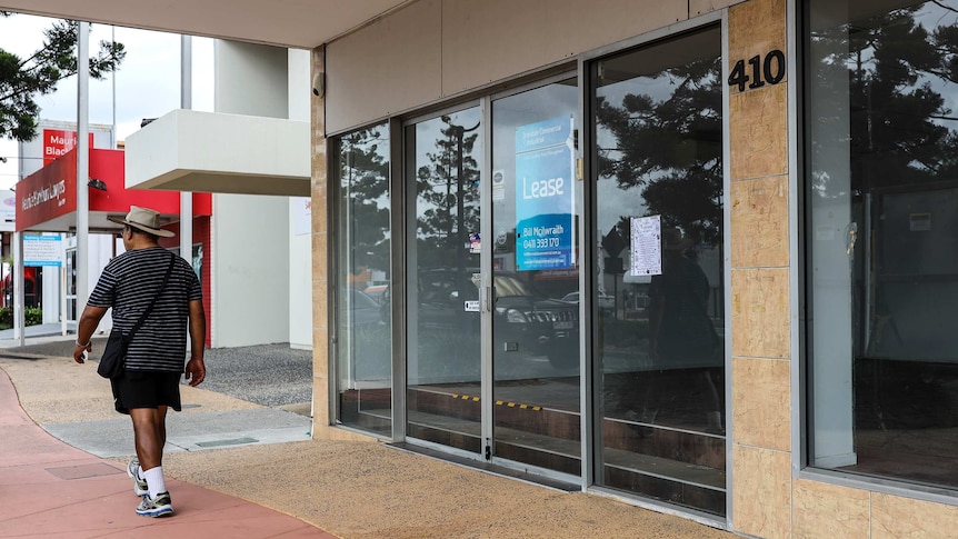 A man walks past an empty shop on Gympie Road at Strathpine with 'Lease' signs in the window.