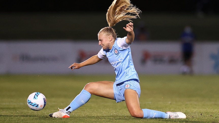 A soccer player wearing light blue stretches for the ball on the grass