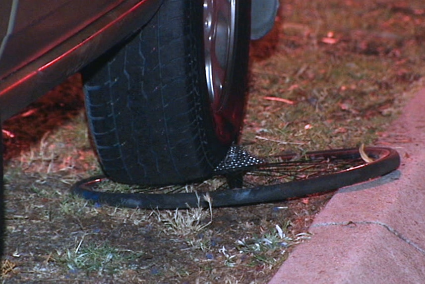 A bike tyre lies crushed under the wheel of a car on a road verge.