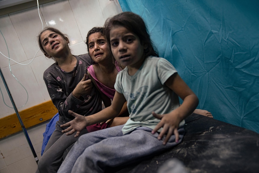 Three children sit on a hospital bed, visibly upset