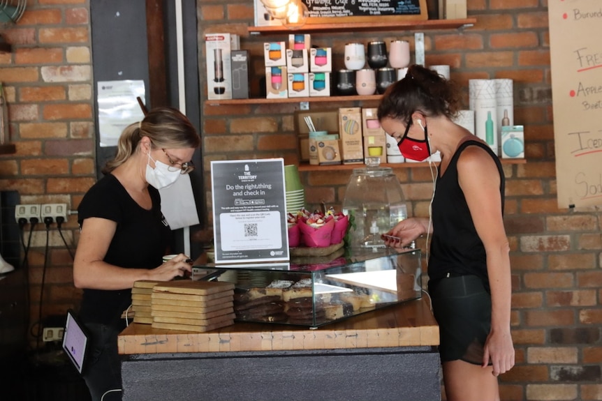 A woman wearing a mask inside a cafe serves a customer, also wearing a mask.
