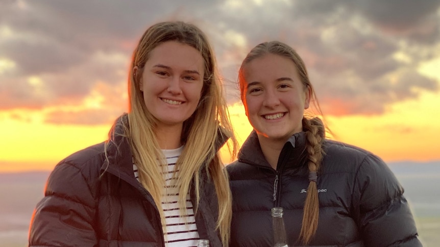 Two women smiling with a sunset behind them