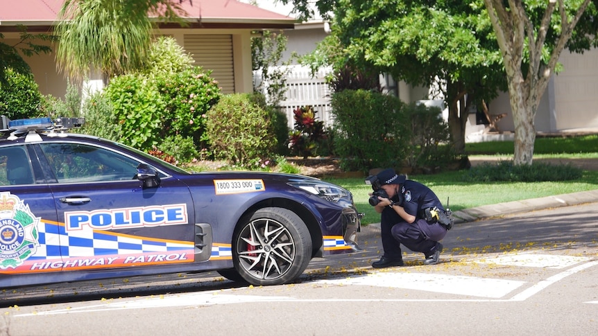 a police officer kneels down taking a photo of the front of a marked highway patrol police vehicle parked in a suburban street