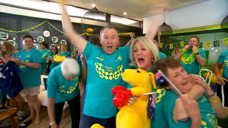 A man with his arms in the air and a woman crying holding a yellow kangaroos and an Australian flag