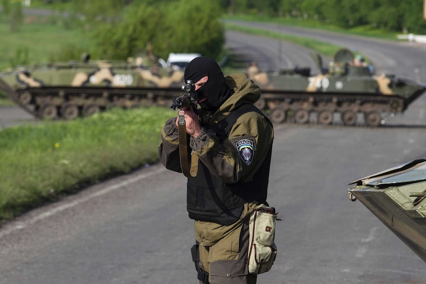 Ukrainian soldier points his weapon at approaching car
