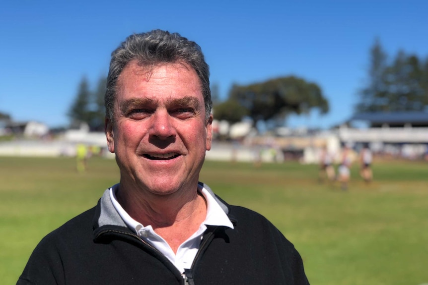 Head and shoulders photo of John Shadbolt standing in front of blue sky and green grass