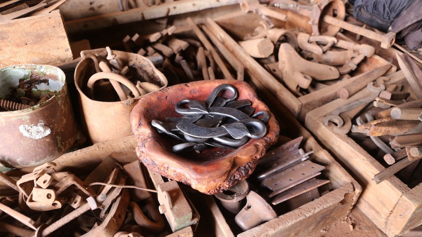 A bowl of handmade cheese knives sits on a table of blacksmithing equipment.