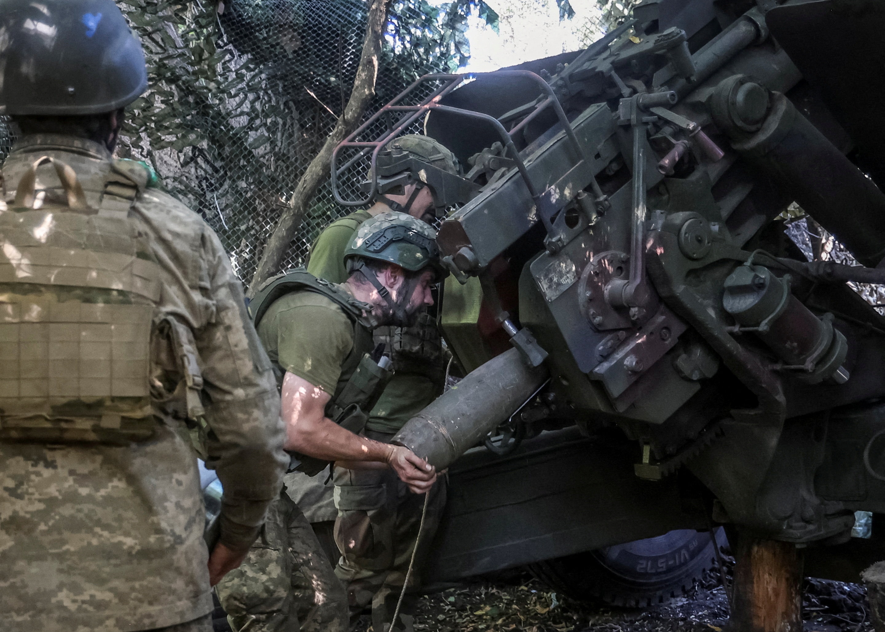 Ukrainian soldiers in military fatigues load a shell into a howitzer cannon.