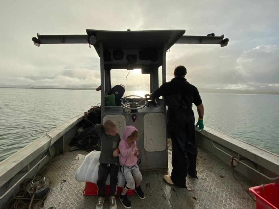 a man drives a boat while two children sit at his feet