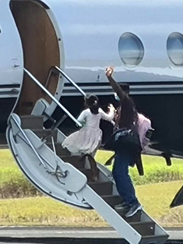 A man and his daughter walk up the steps of a plane waving.