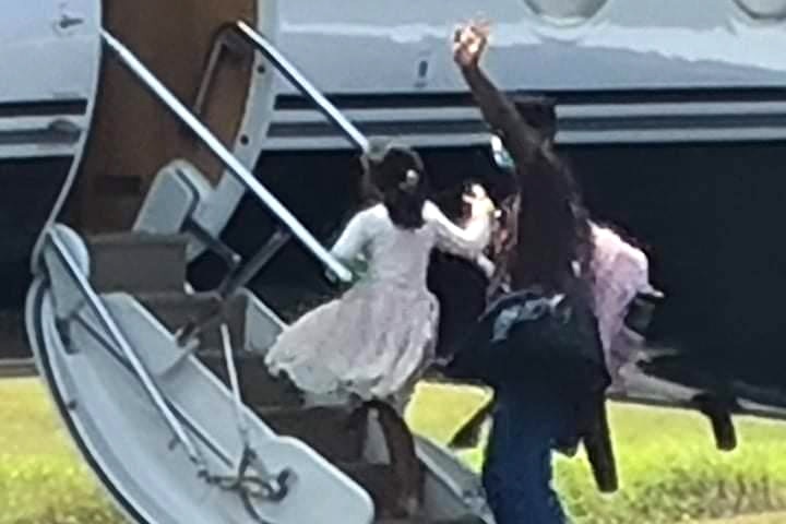 A man and his daughter walk up the steps of a plane waving.