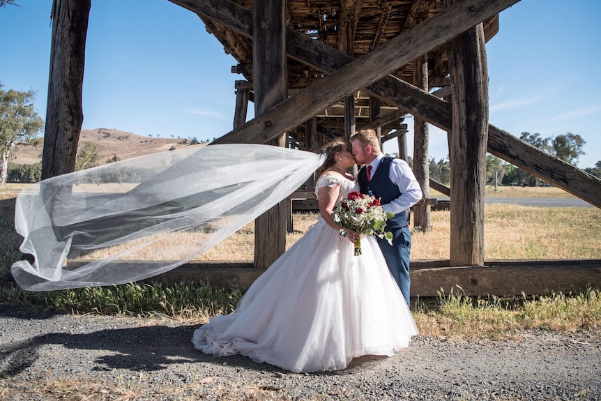 A bride and groom kiss under a timber bridge.