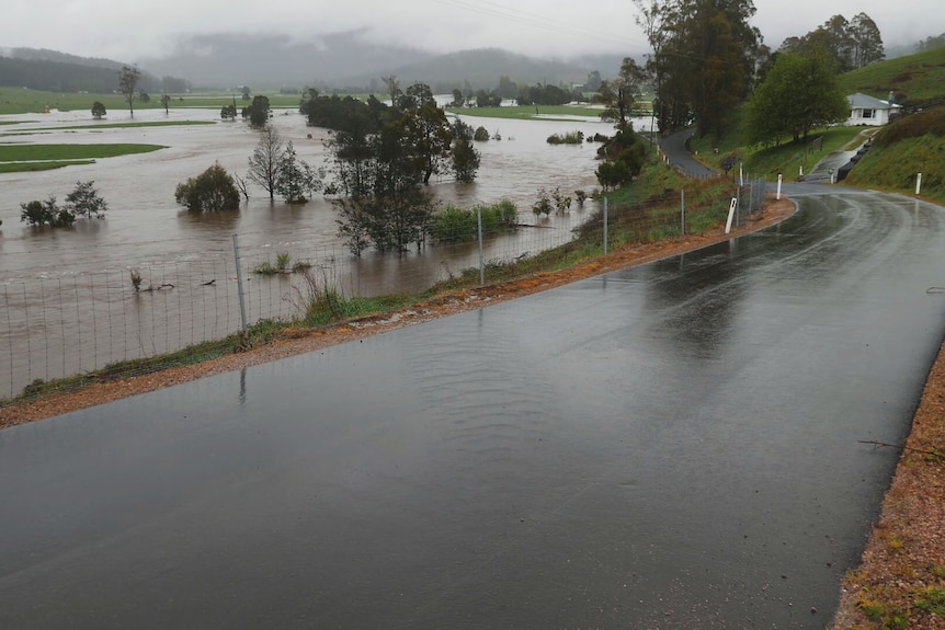 Une route mouillée passe devant une ferme complètement inondée.