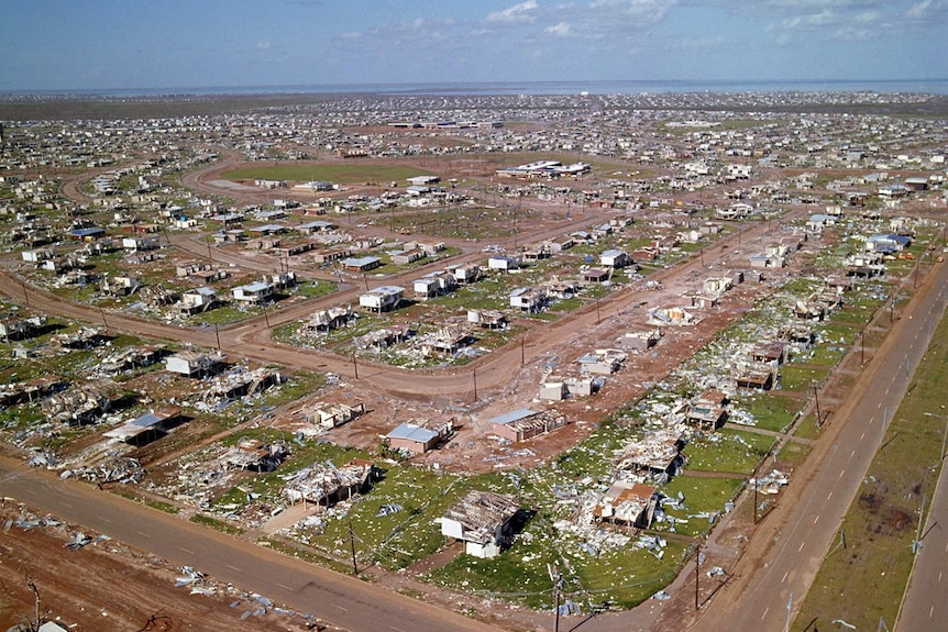 An aerial photo of houses badly damaged after a cyclone, on a sunny day. 