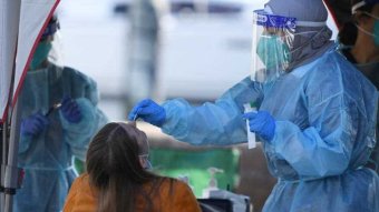 A woman in a hazmat suit swabs a woman to test for coronavirus.