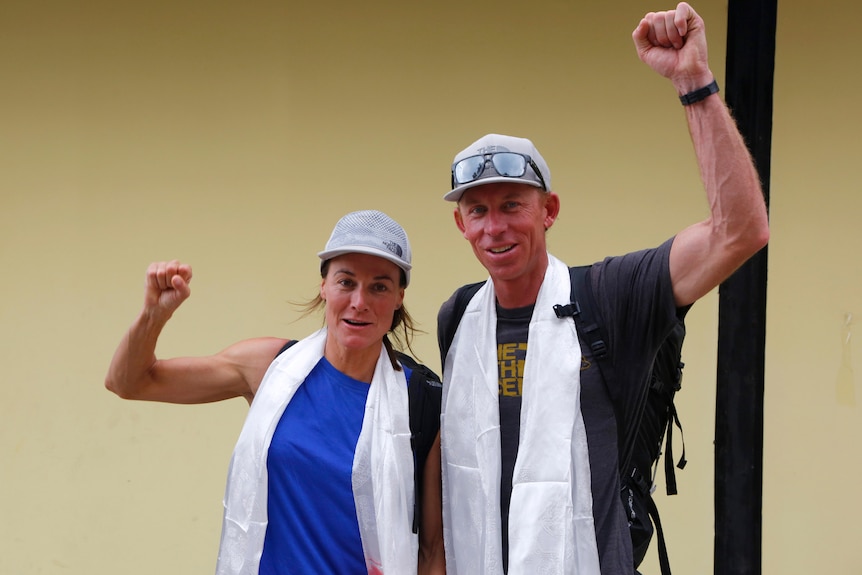 A fit-looking couple raise their fists in the air while wearing caps and backpacks.