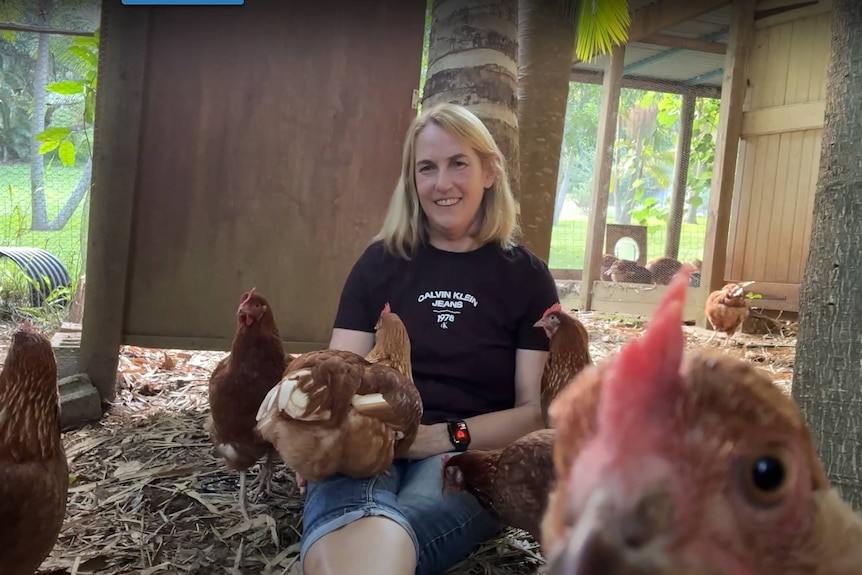 woman sitting with hens in a coop