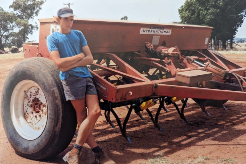 Greg leans against a large piece of farming equipment in a photo from the 90s.