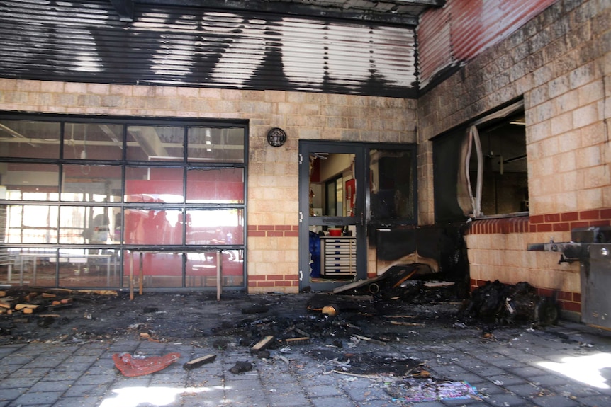 A fire-damaged school courtyard with damaged doors, charred walls and rubble one the ground.