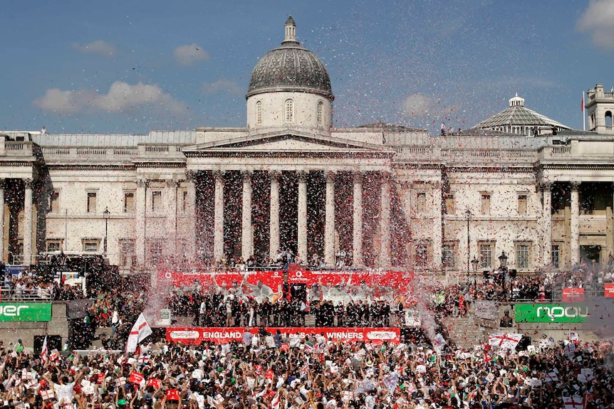A huge crowd is gathered at Trafalgar Square cheering and celebrating England's cricketers who are on the stage. 