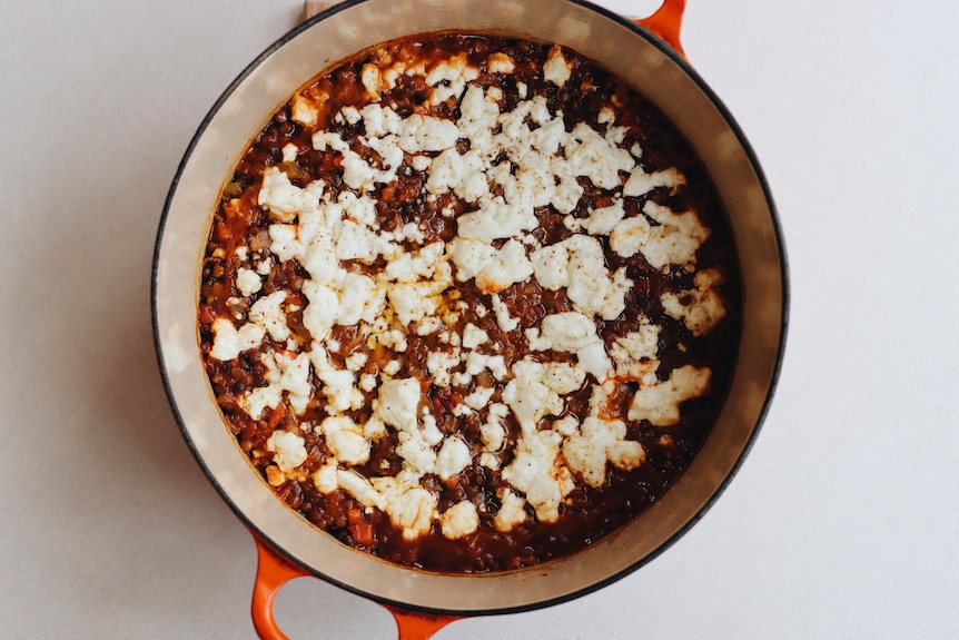 A birds-eye view of a Dutch-oven pot filled with lentils and topped with feta cheese and herbs.