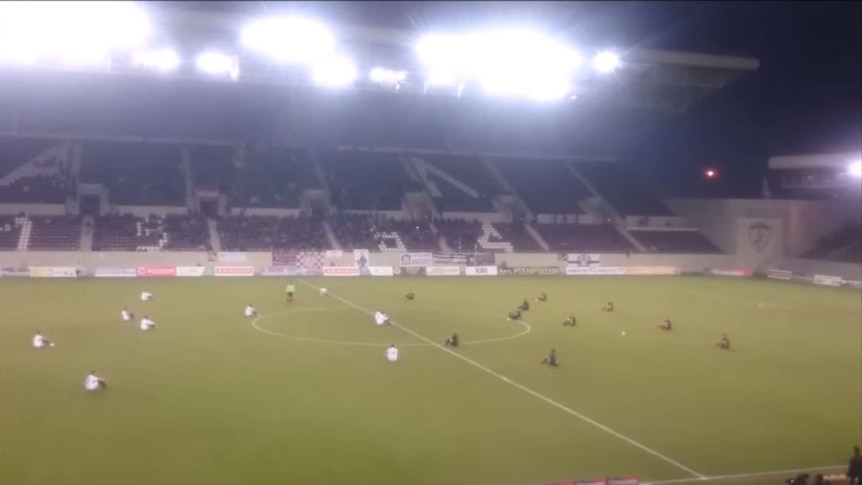 Screenshot of video of Greek soccer players and coaches making sit-down protest supporting refugees.