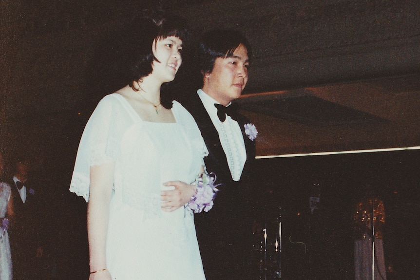 A 1980s photograph of a man and woman linking arms wearing formal attire.