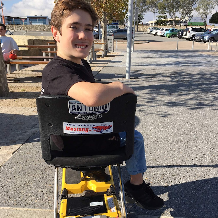 Coby Antonio sits on his yellow scooter looking over his shoulder and the chair.