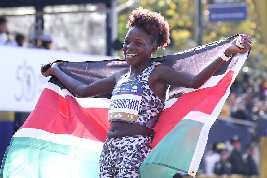 Peres Jepchirchir holds a flag over her shoulders and smiles