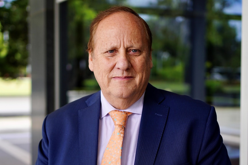 A man in a suit looks at the camera with a serious expression