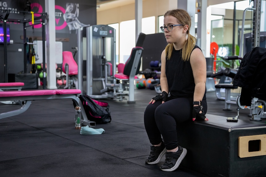 Julie Dickson, a short statured woman, sits on a bench at a gym.