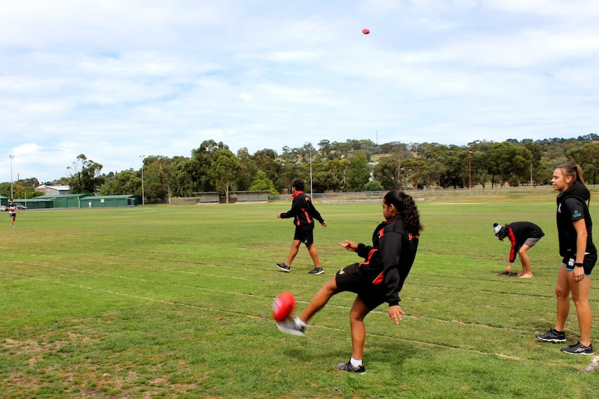 Female student kicks football on Mount Gambier High School oval.