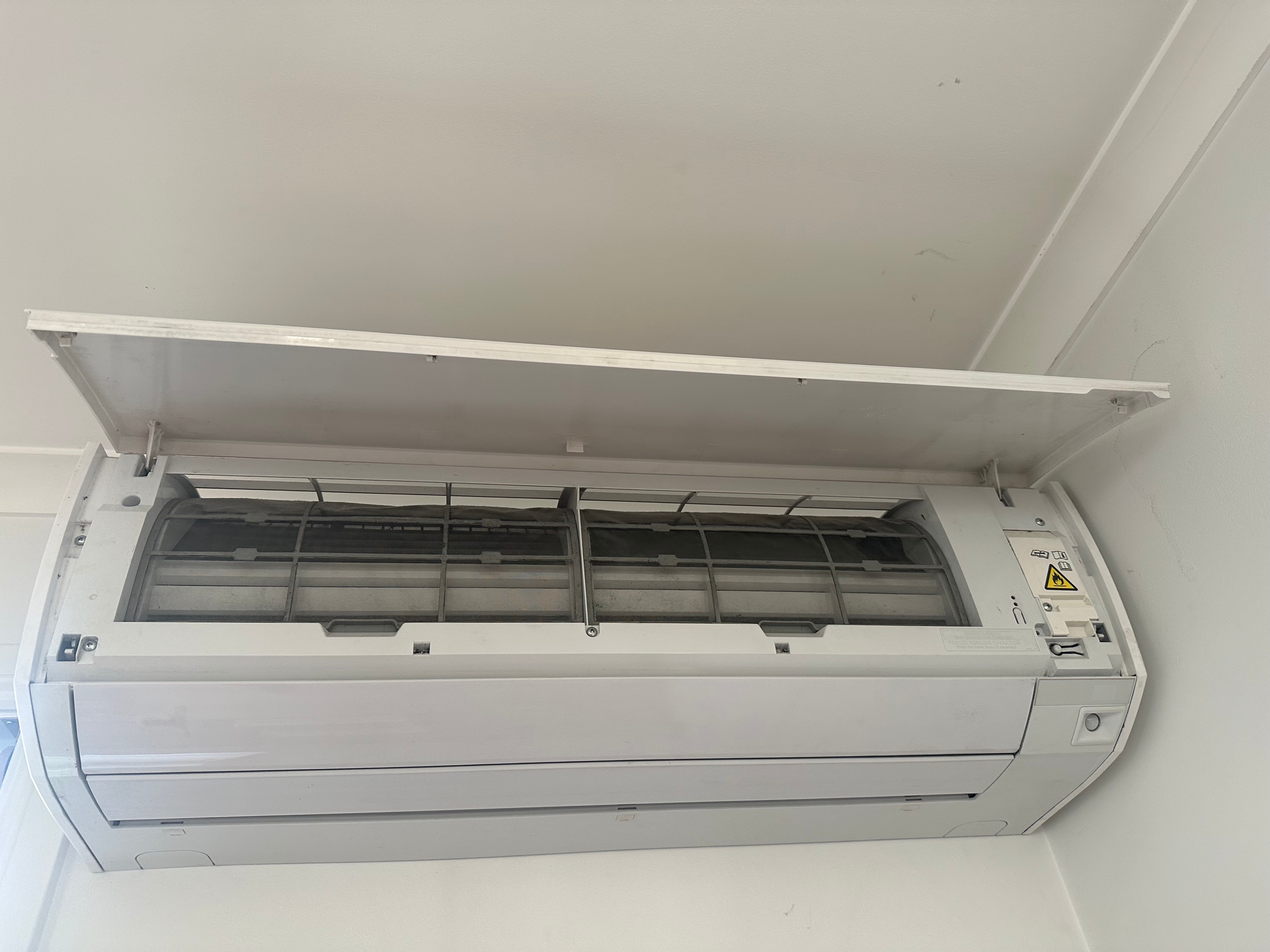 An indoor air-conditioning unit with the cover lifted, revealing internal filters that need to be cleaned every fortnight or so.