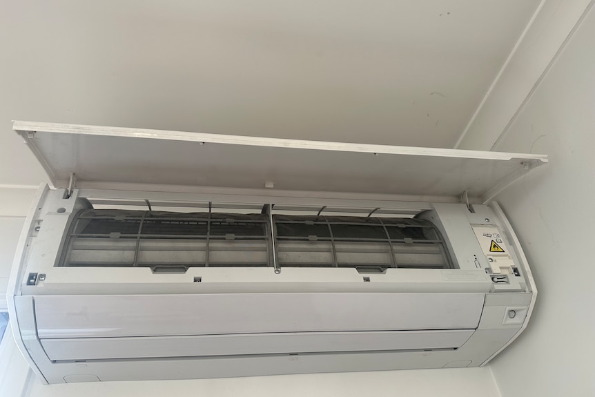 An indoor air-conditioning unit with the cover lifted, revealing internal filters that need to be cleaned every fortnight or so.