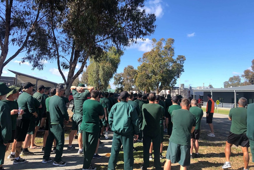 A group of prisoners stand at the starting point of the race, blue skies, shaded area