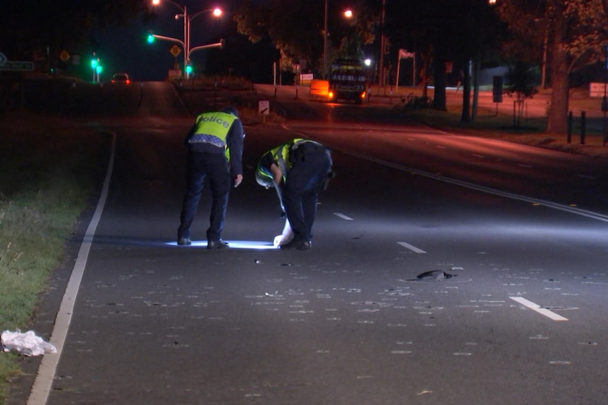 The backs of two police officers examining the scene of a crash.