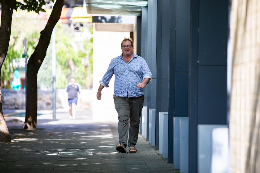 A man in a blue shirt and long pants walks along the street.