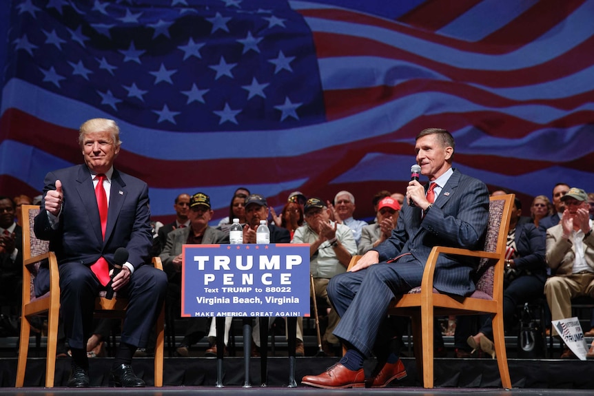 Donald Trump gives a thumbs up as he speaks with  Michael Flynn in front of an audience