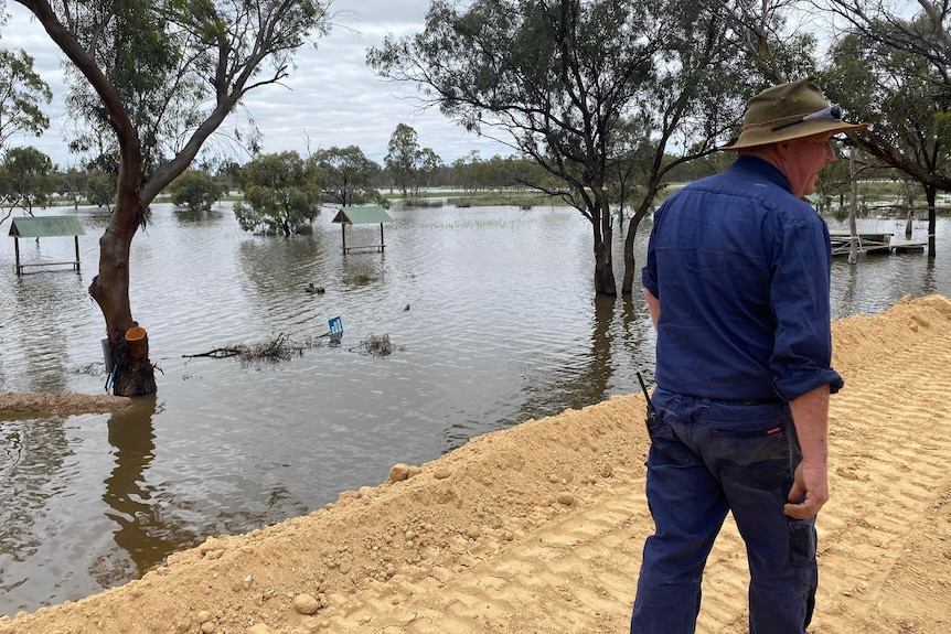 A man wearing a hat on a levee bank with floodwater in the background.