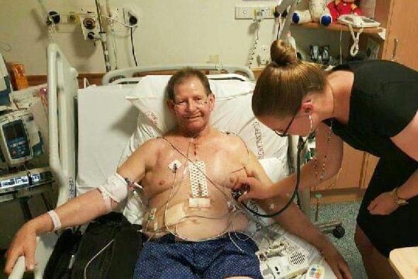 Colin Manderson lies in a hospital bed receiving care from a nurse after having a heart transplant.