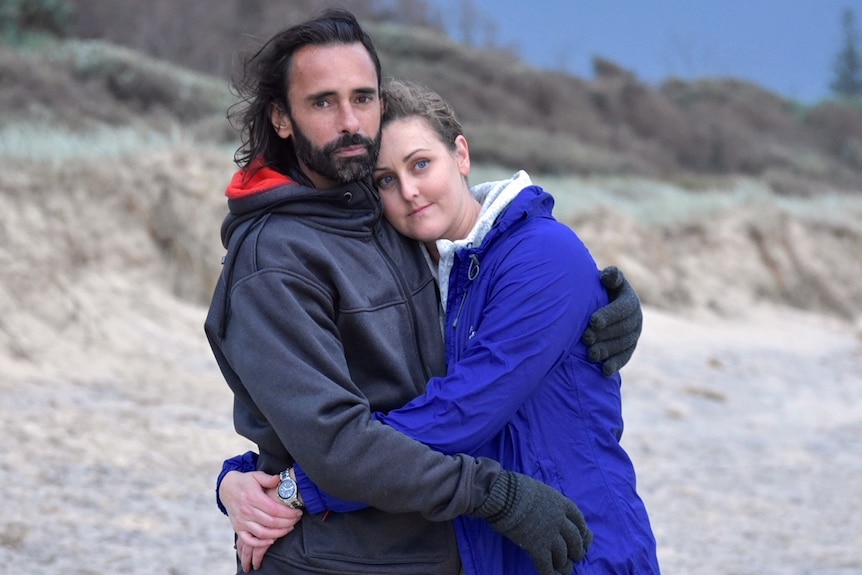 Sam and Sarah Stefanaras holding each other on a windswept beach