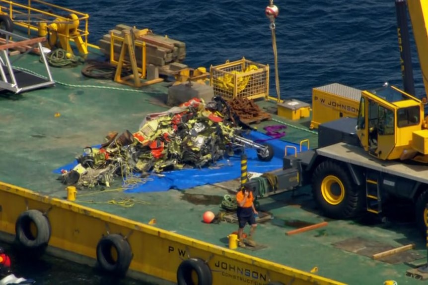 A pile of apparent wreckage on a yellow barge in the middle of the sea.