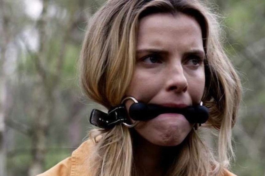 In a still from the movie, a woman is shown gagged with a black belt.