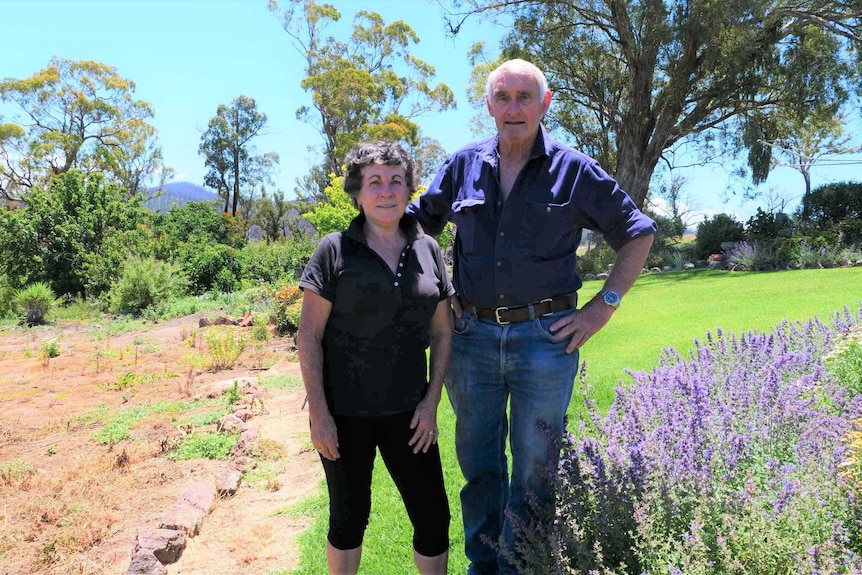 A middle aged couple stand in a pretty bush garden setting